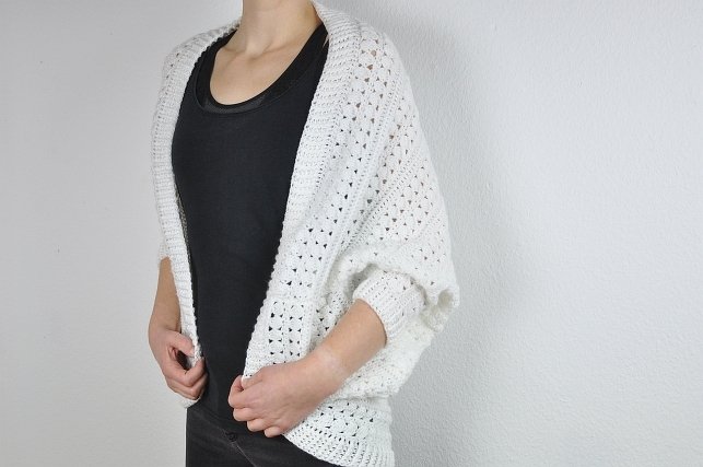 Person wearing a white crocheted shrug with a lacy openwork pattern over a black top.