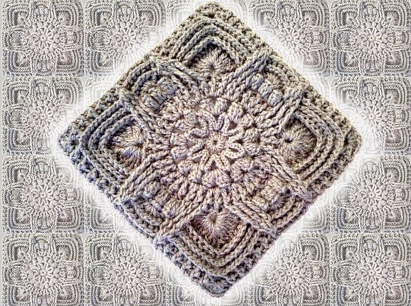 Hellgraues gehäkeltes Granny Square mit reliefartigem Blumenmittel, diagonal ausgerichtet.