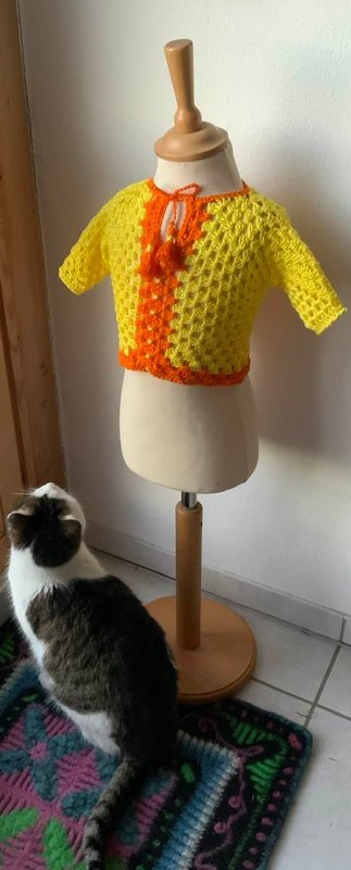 Gelbes gehäkeltes Kinder-Top mit orangefarbener Kante auf Schaufensterpuppe, kurze Ärmel und Halsbändchen