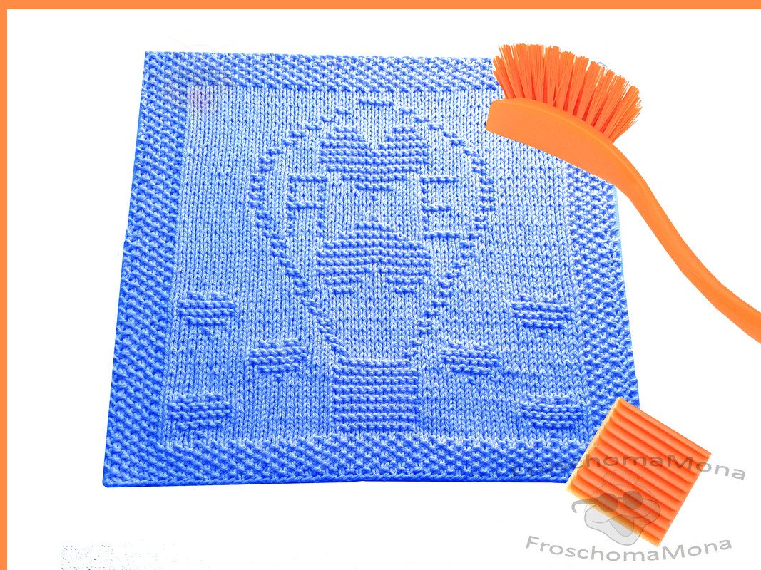 Blaues quadratisches Stricktuch mit Heißluftballon- und Wolkenmuster, daneben orangefarbene Bürste und Scheuerpad