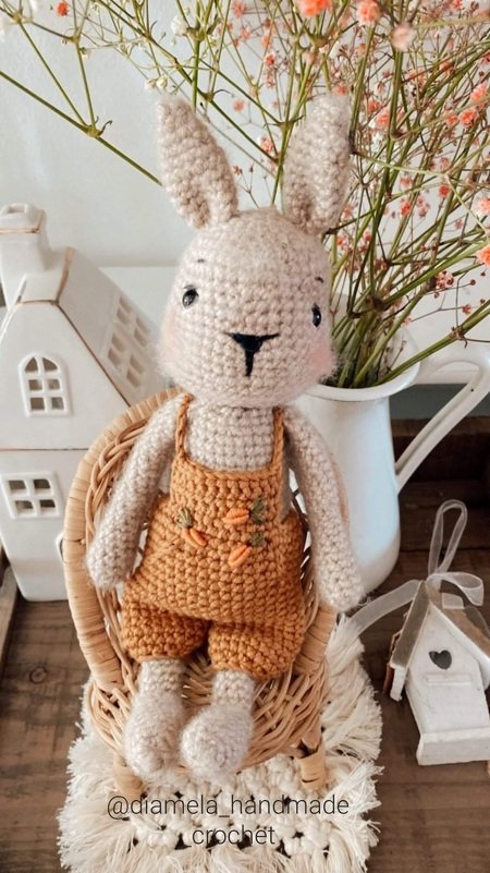 Gehäkelter Amigurumi‑Hase mit langen Ohren und senffarbener Latzhose, sitzend