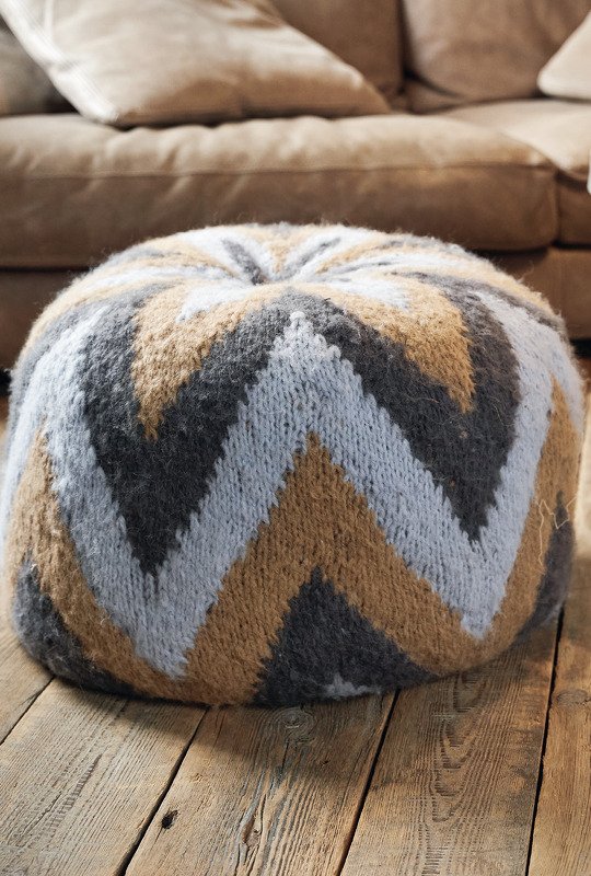 Runder gestrickter Pouf im Chevronmuster in Beige und Grau auf Holzdielen