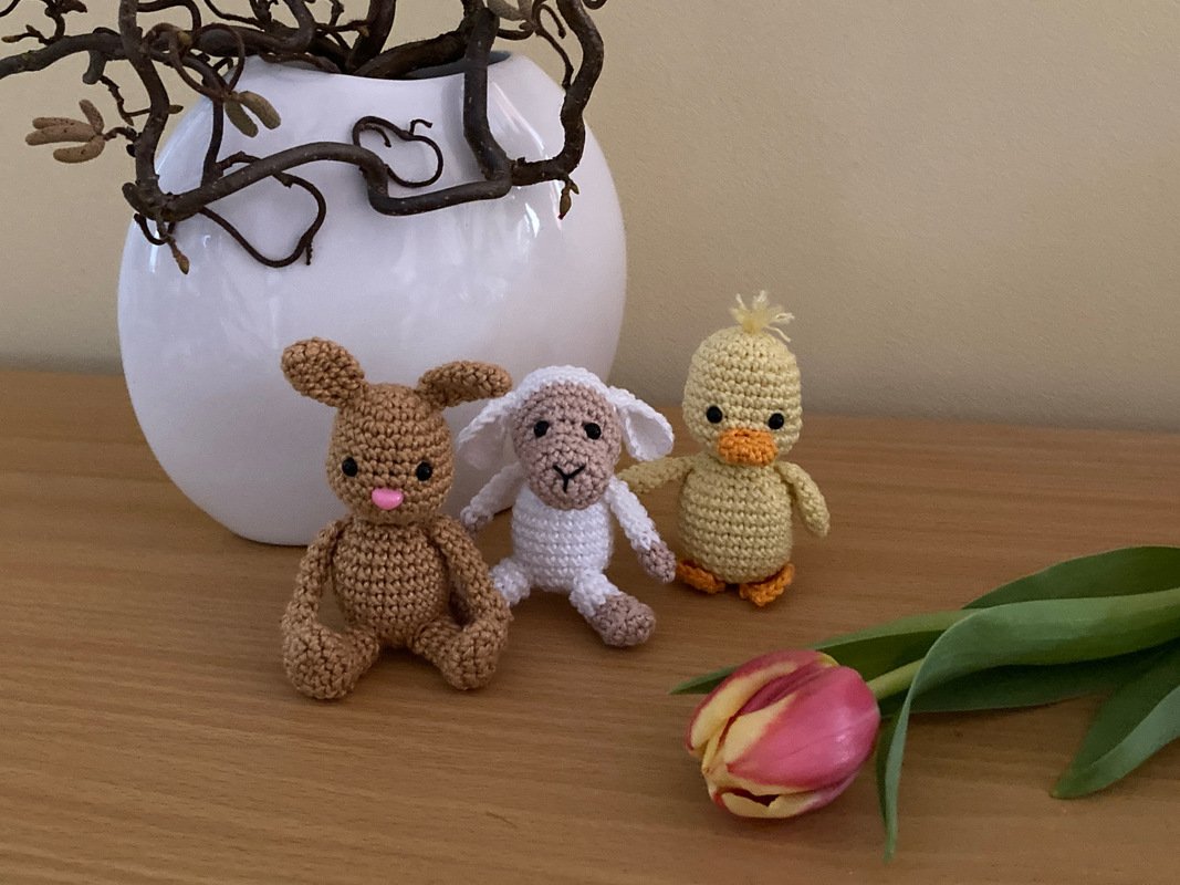 Gehäkelte Amigurumi Hase, Lamm und Küken nebeneinander vor weißer Vase und Tulpe