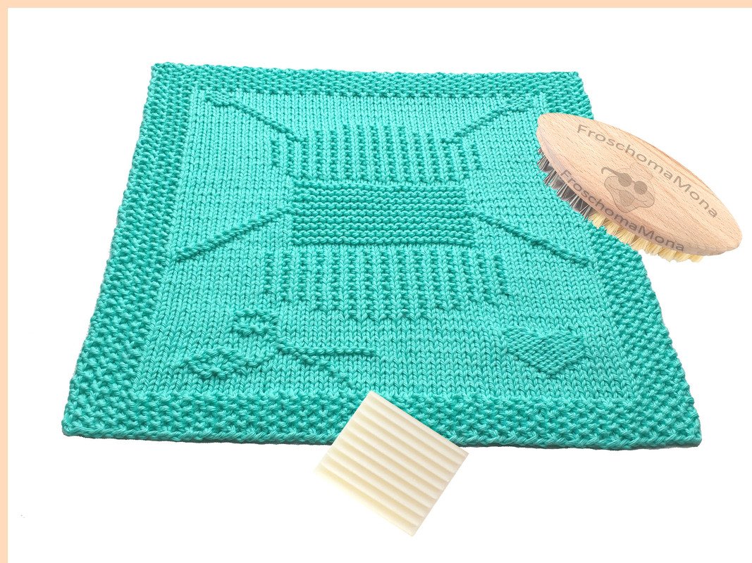 Mintgrünes gestricktes Spültuch mit Reliefmustern, neben Holzbürste und Reinigungspad