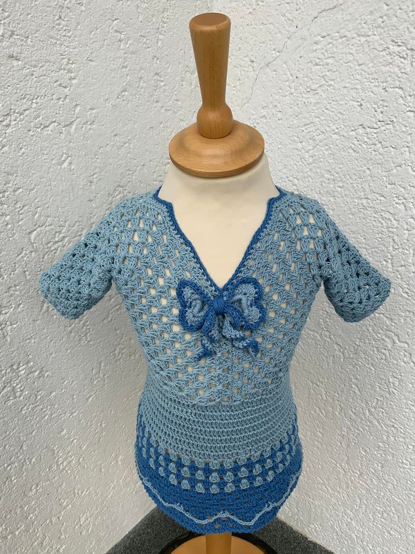 Hellblaues gehäkeltes Kinderkleid mit V-Ausschnitt und Schleife auf Schaufensterpuppe