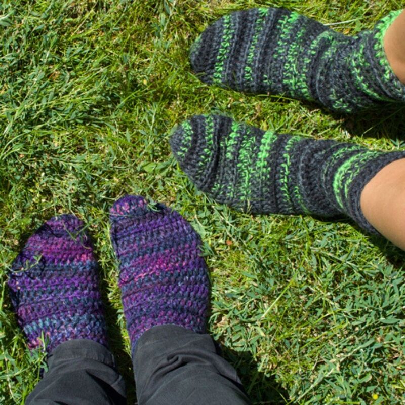 Zwei Paar verschiedenfarbige gehäkelte Socken auf sattem Grün