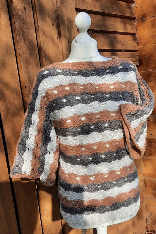 Gestrickter Damenpullover mit horizontalen Streifen und Lochmuster auf einer Schaufensterpuppe vor Holzwand.