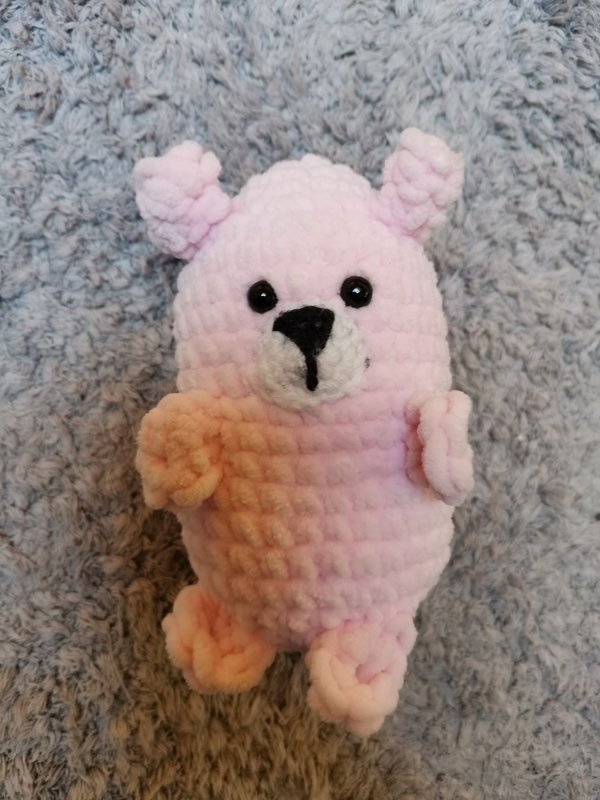 Gehäkelter rosa Amigurumi-Teddy aus plüschigem Garn auf grauem Untergrund