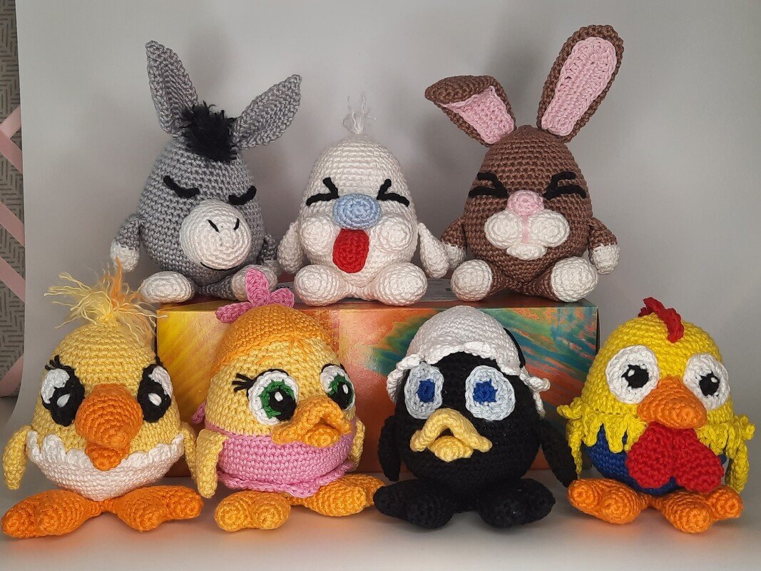 Sieben gehäkelte Amigurumi-Figuren in zwei Reihen: Esel, Fantasiefigur, Hase und vier verschiedene Küken/Hühner.