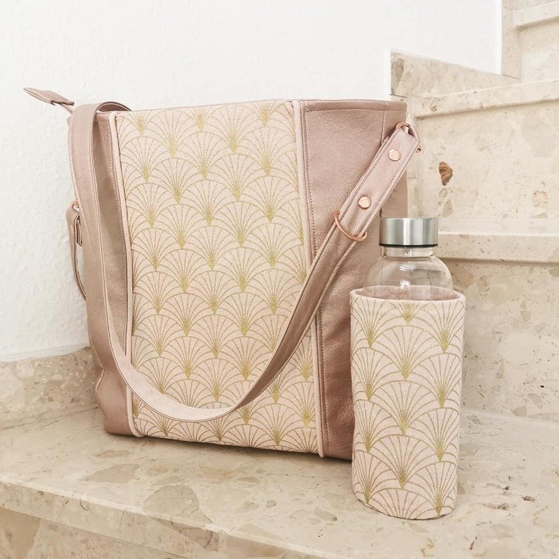 Roségoldene Umhängetasche mit goldenem Fächermuster und passender Flaschenhülle auf Marmorstufe