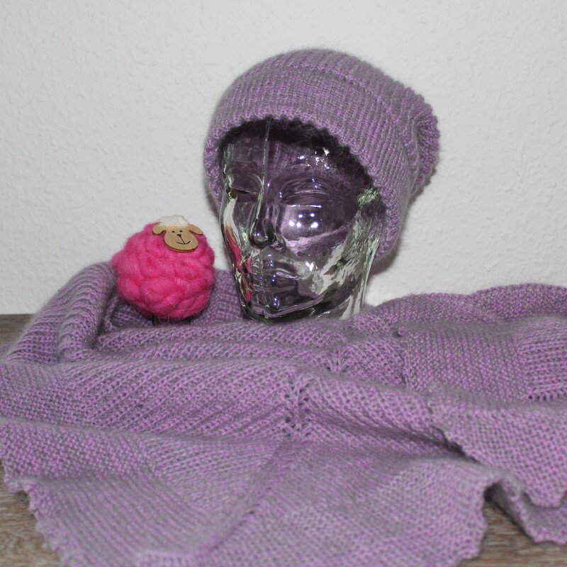 Lila gestrickte Mütze und Schal auf durchsichtigem Schaufensterkopf neben einer pinken Wollschaf-Dekoration