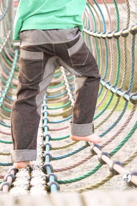 Rückansicht einer genähten Kinderhose mit Kniepatches und aufgesetzten Taschen, Kind barfuß auf einem Kletternetz