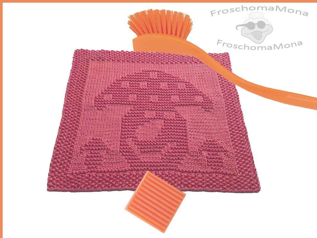Rosa gestricktes Spültuch mit Pilzmotiv, orangefarbene Spülbürste und Seifenstück auf hellem Hintergrund.