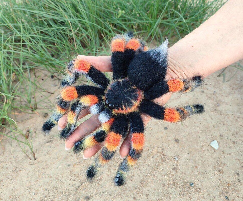 Hand holding a palm-sized crocheted spider amigurumi in black, orange and gray fuzzy yarn