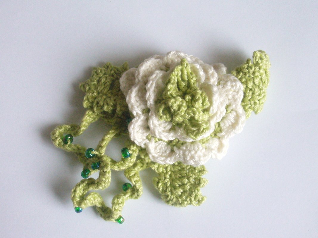 Mehrlagige gehäkelte Blüte in Cremeweiß und Hellgrün mit Blättern und perlengeschmückten Ranken