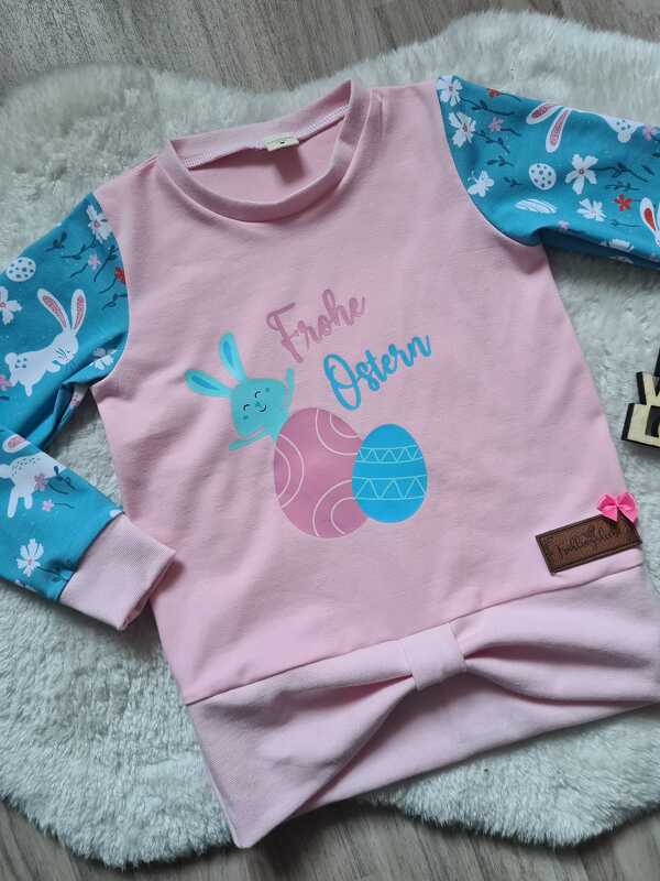 Zentral platzierter mehrfarbiger Osterplott mit Schriftzug, Hase und Eiern auf rosa Kinderpullover