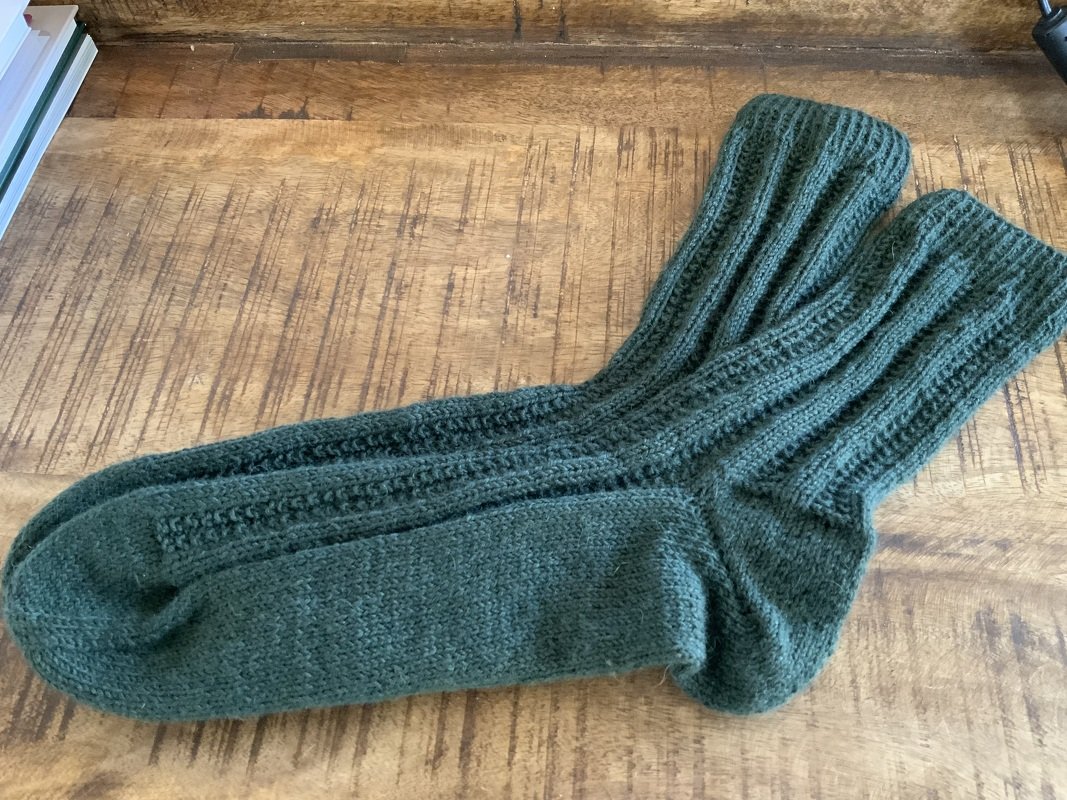 Dunkelgrüne gestrickte Socken mit Rippenmuster auf einer Holzoberfläche.