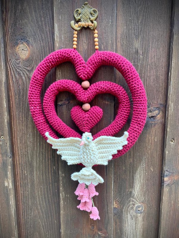 Gehäkelter Türkranz aus drei pinken Herzen mit Holzperlen, unten eine weiße Taube und rosa Blüten vor einer Holztür
