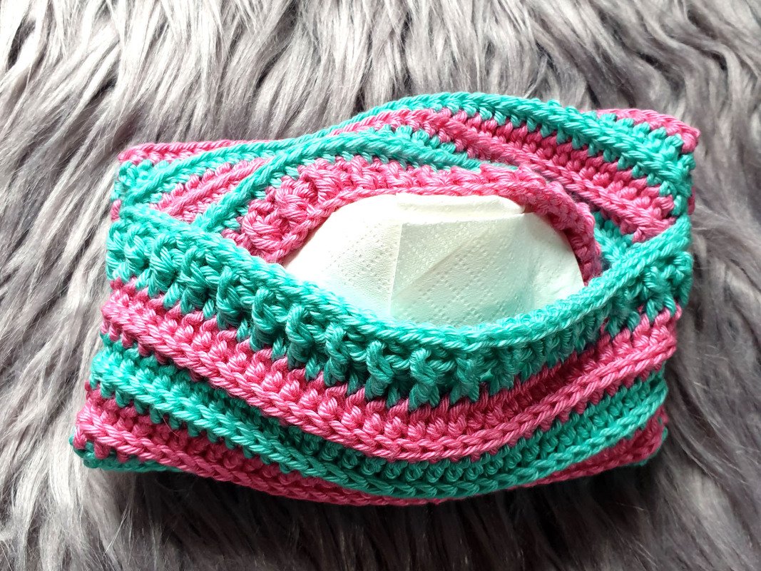 Gehäkelte Taschentuchhülle in Rosa und Türkis auf grauem Fell