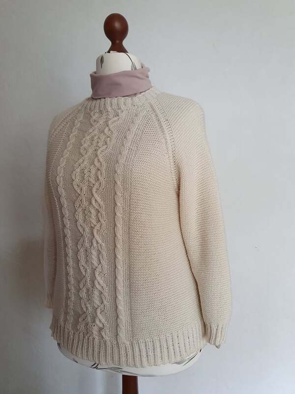 Beigefarbener gestrickter Pullover mit zentralem Zopfmuster auf einer Schneiderpuppe.