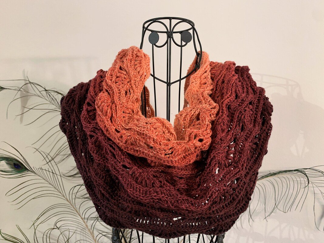 Ombré crocheted infinity cowl in coral and burgundy on a wire mannequin.