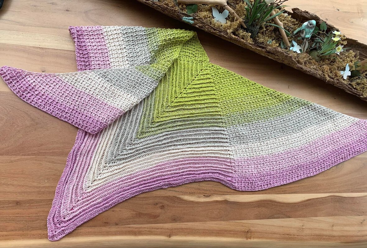 Gehäkeltes Dreieckstuch mit Farbverlauf in Lila, Beige, Grau und Limettengrün, ausgebreitet auf einer Holzoberfläche.