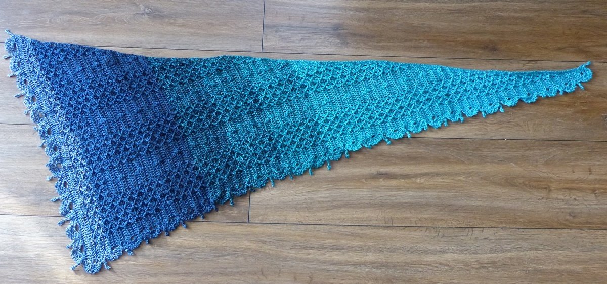 Gehäkelter dreieckiger Drachenschwanz-Schal mit blau-türkis Farbverlauf und Muschelkante auf Holzboden