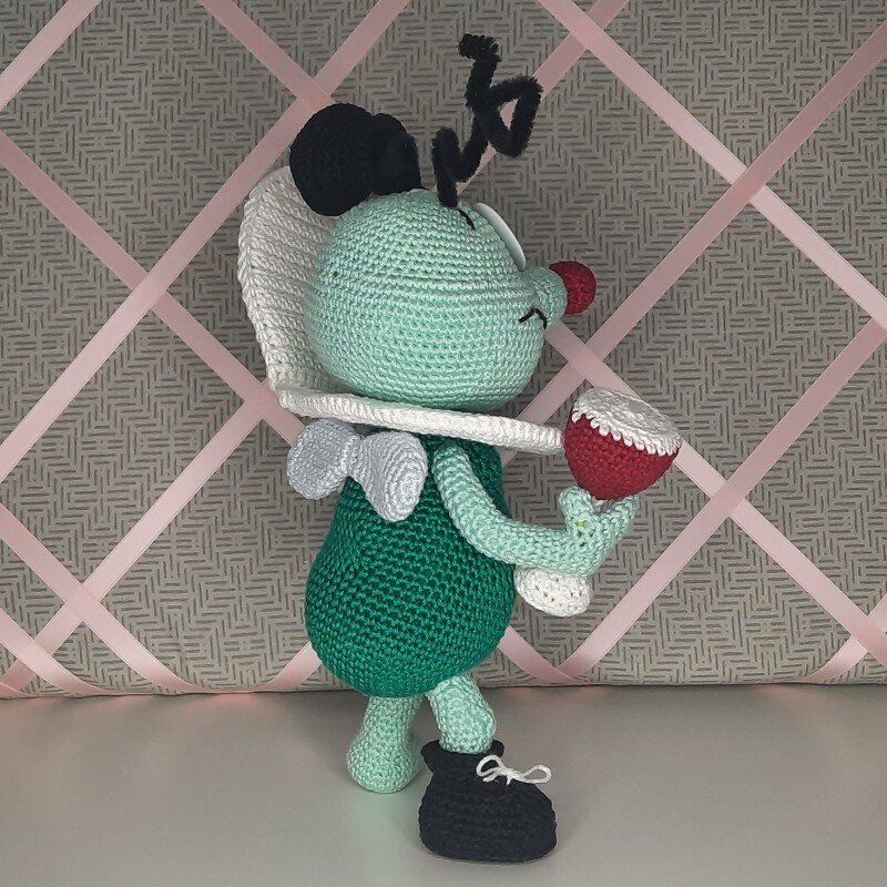 Gehäkeltes grünes Käfer-Amigurumi mit weißem Rüschenkragen, schwarzen Antennen und rotem Becher
