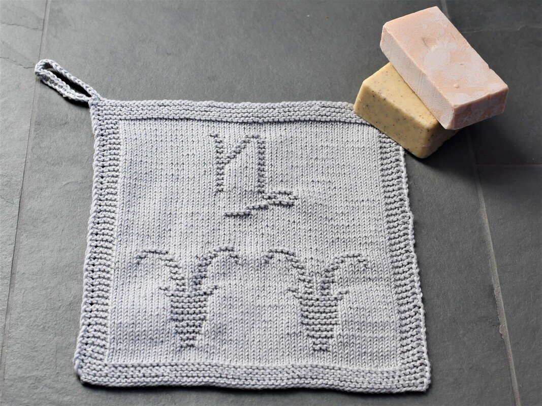 Light grey knitted square washcloth with textured candle motif and hanging loop