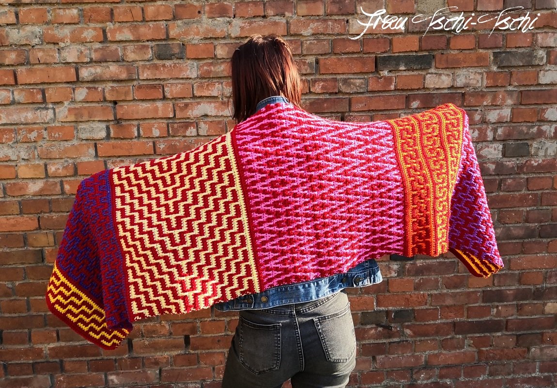 Rückenansicht einer Person, die ein farbenfrohes, gehäkeltes Patchwork-Tuch mit grafischen Mustern ausbreitet