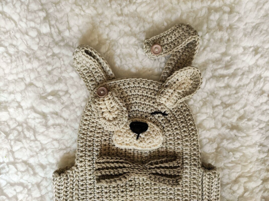 Beige crocheted baby overall with winking dog face, floppy ears and bow tie