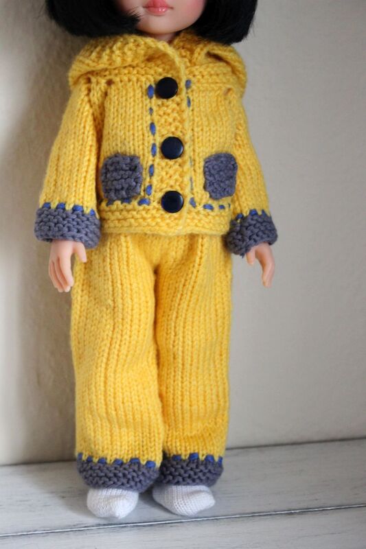 Doll wearing a yellow hand-knitted hooded jacket with three buttons and matching yellow pants with grey trim
