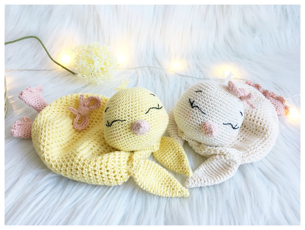 Two crocheted baby loveys — yellow chick and cream bunny with embroidered closed eyes on white faux fur and warm fairy lights