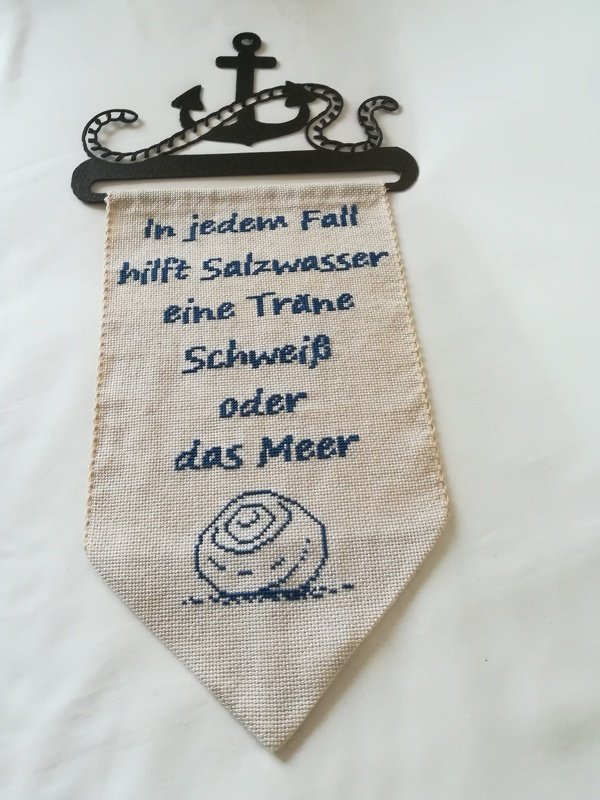 Heller Stoffwimpel mit blauem Kreuzstich‑Spruch und Muschelmotiv an Anker‑Halterung