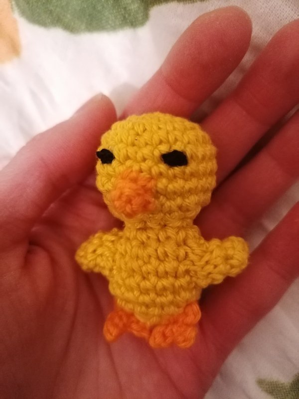 Gehäkeltes gelbes Küken mit orangefarbenem Schnabel und Füßen in einer Hand