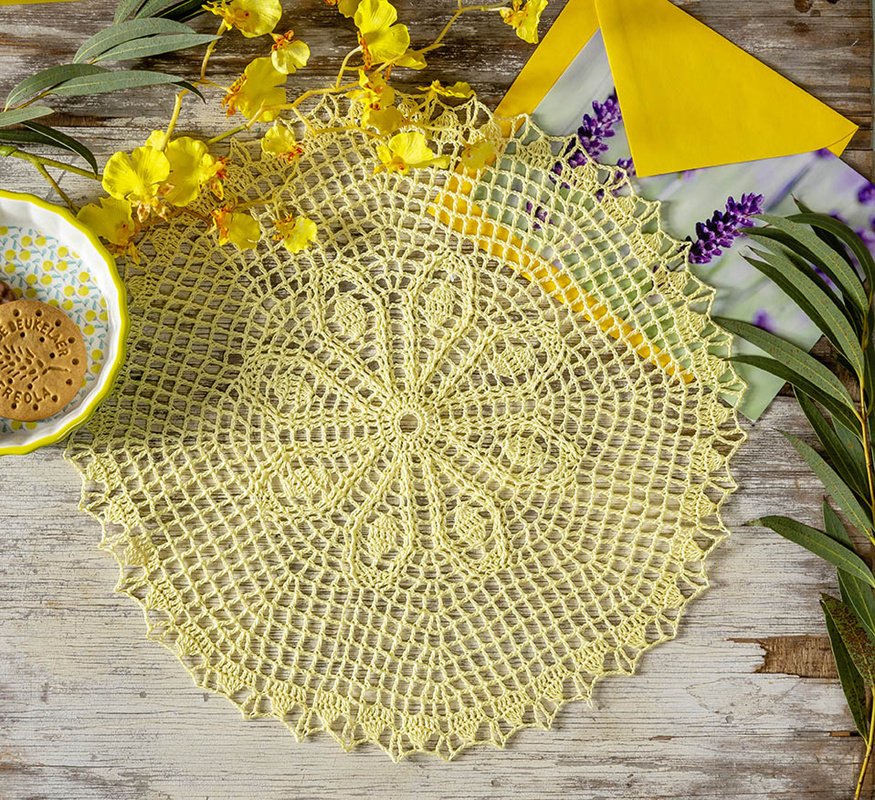 Gelbes rundes gehäkeltes Deckchen mit Blumenmuster auf hellem Holztisch