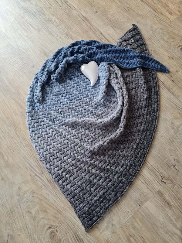 Gestricktes Dreieckstuch in Blau-Grau-Verlauf auf Holzfußboden mit weißem Herz.