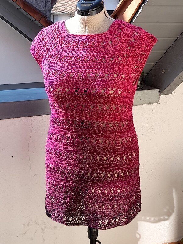 Frontansicht eines sommerlichen, ärmellosen Häkelkleids in Pink mit Ajourmuster und dunklerem Saum