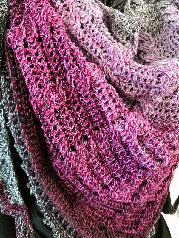 Close-up of a pink-to-grey gradient triangle crochet shawl showing lacy open stitches and textured rows