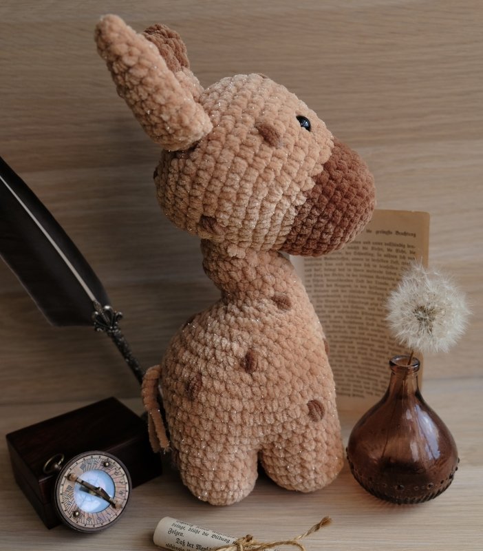 Gehäkelte Giraffe aus plüschigem Garn mit braunen Tupfen, daneben Federkiel, Kompass und altes Papier