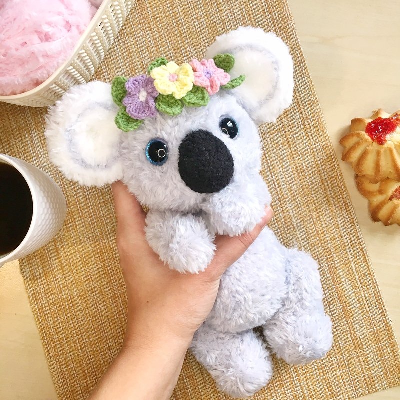 hand holding a gray crocheted koala amigurumi wearing a pastel flower crown
