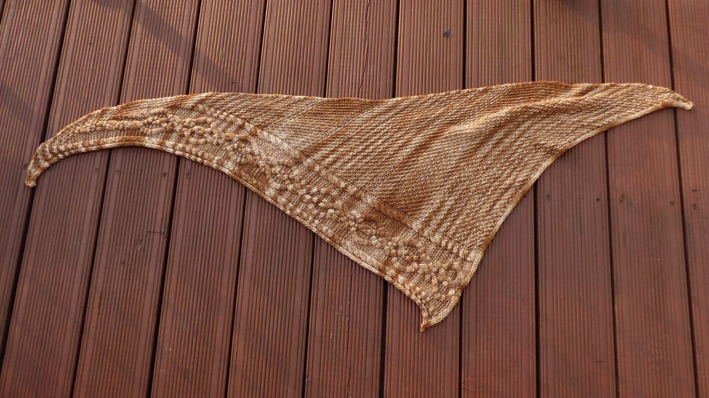 Gestricktes braun-beiges Dreieckstuch mit Zopfmuster auf Holzdielen