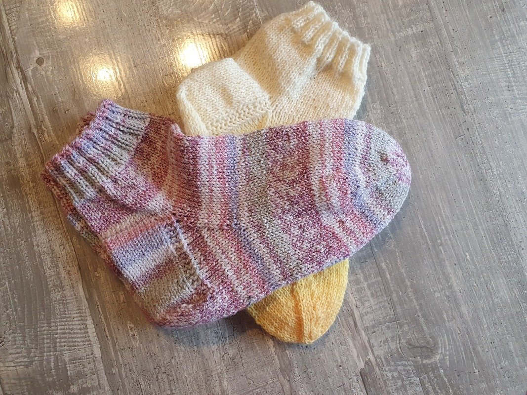 Drei gestrickte Damensocken in Pastell- und Uni-Farben auf hellem Holzboden