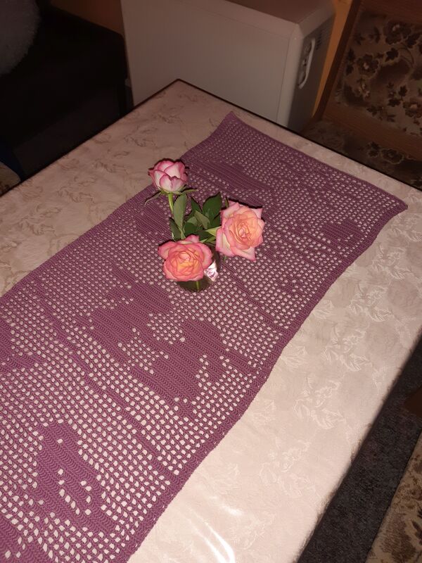 Handgehäkelter lila Tischläufer mit Herzmuster und drei rosafarbenen Rosen.
