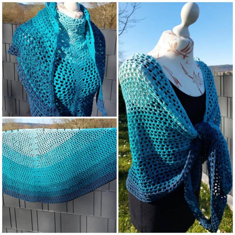 Halbrundes gehäkeltes Tuch in Türkis‑ und Blautönen mit Farbverlauf und offenem Lochmuster, auf einer Schaufensterpuppe drapiert.