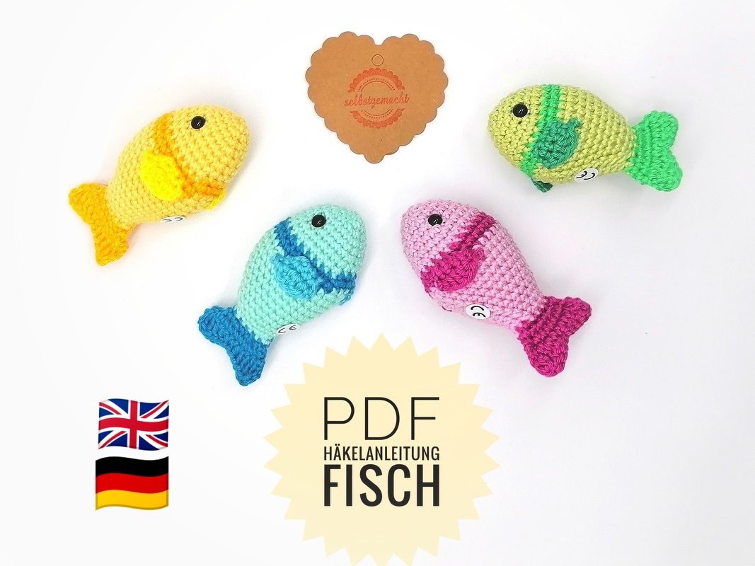 Four small crocheted fish in yellow, teal, pink, and lime green, arranged on a white background with a central starburst label reading 'PDF Häkelanleitung Fisch' and flags for the UK and Germany.