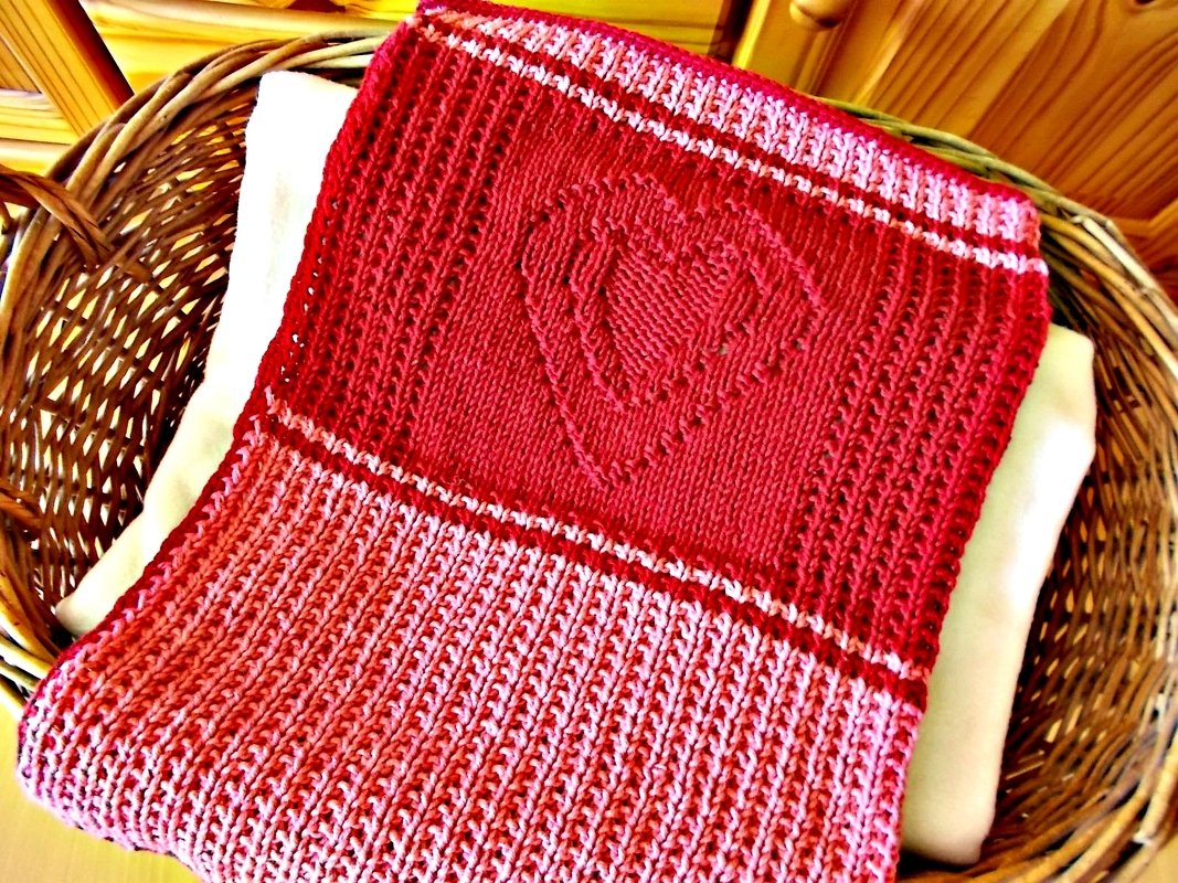 Gestrickte Babydecke rot-rosa mit Herzmuster im Weidenkorb