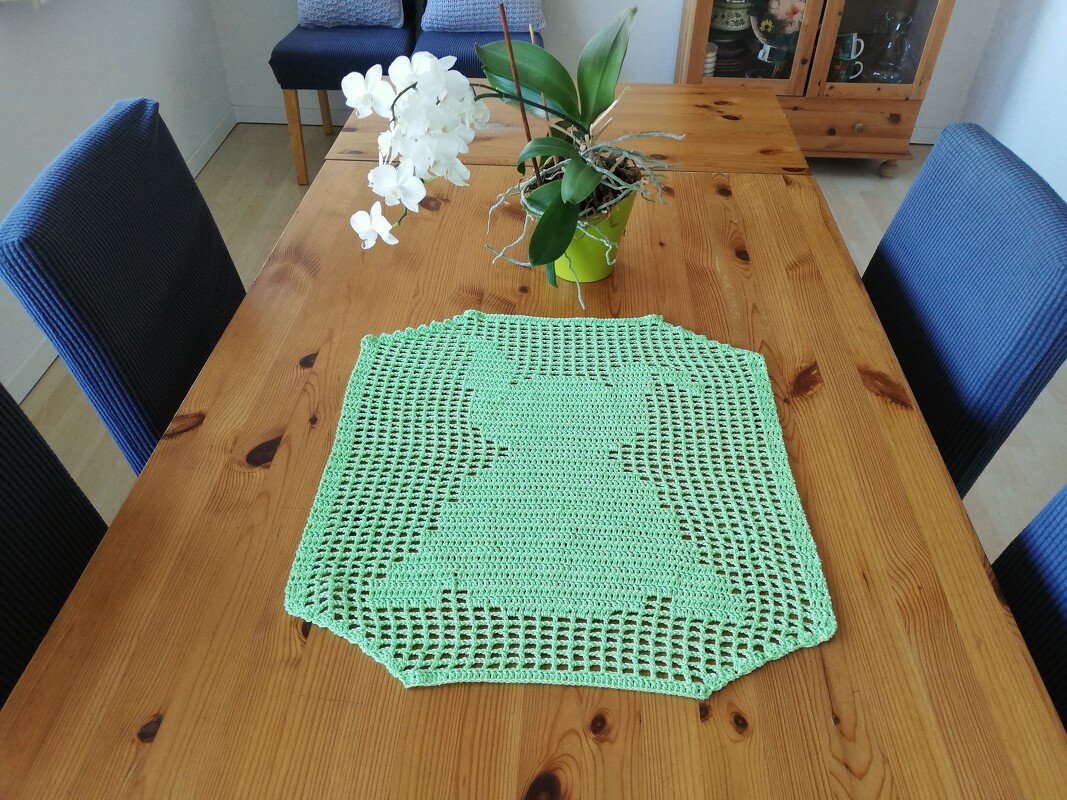 Hellgrünes gehäkeltes Deckchen mit Hasensilhouette auf Holztisch