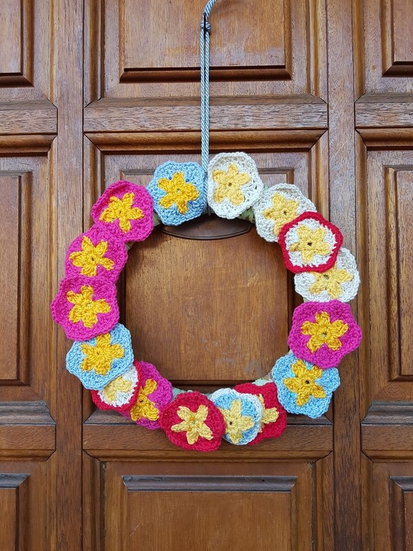 Runder Kranz aus bunten, gehäkelten Blumenapplikationen an einer Holztür