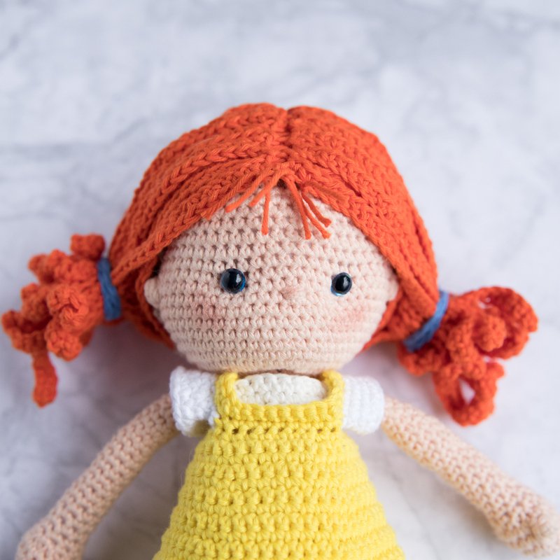 Nahaufnahme einer Amigurumi-Häkelpuppe mit roten Zöpfen und gelbem Kleid